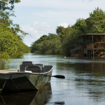 Embarcação navegando em rio da região de Três Lagoas, com vegetação às margens e estrutura turística ao fundo