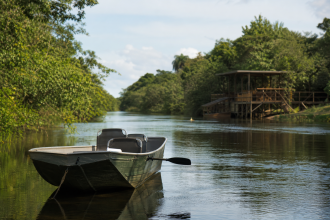 Embarcação navegando em rio da região de Três Lagoas, com vegetação às margens e estrutura turística ao fundo