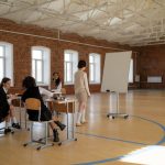 Estudantes uniformizados participam de uma aula com a professora em uma sala de aula.