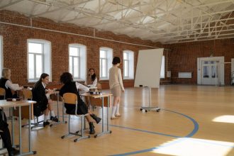 Estudantes uniformizados participam de uma aula com a professora em uma sala de aula.