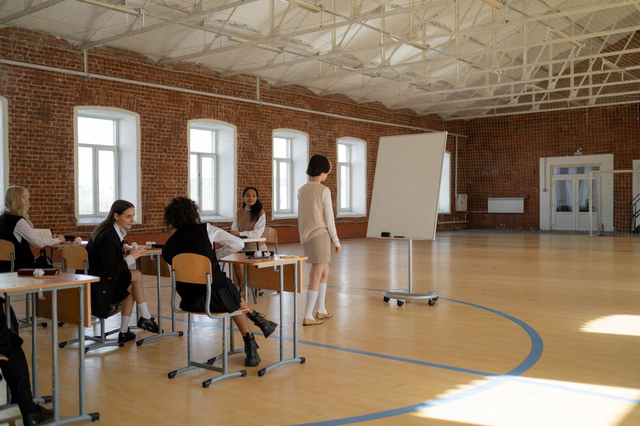 Estudantes uniformizados participam de uma aula com a professora em uma sala de aula.