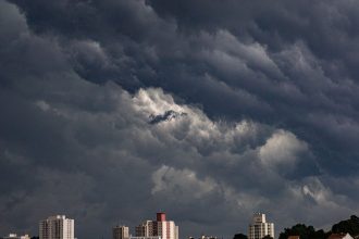 Nuvens escuras de tempestade se acumulam sobre edifícios de uma área urbana.