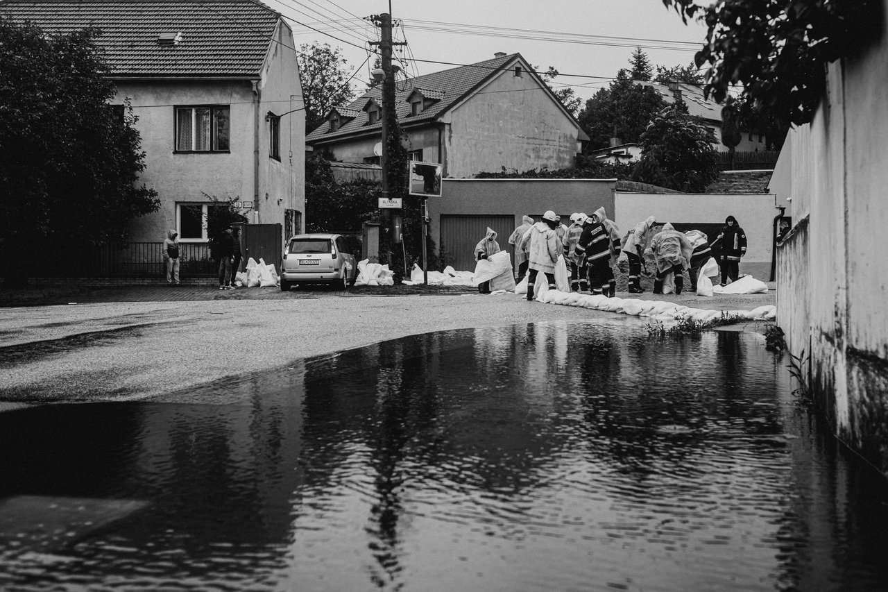 Voluntários usando roupas de proteção montam barreiras de sacos de areia durante um alagamento urbano.